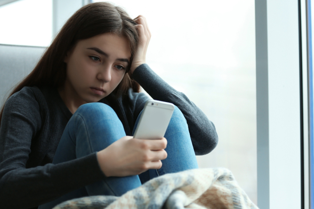 A young girl looking down or shamed while looking at her phone