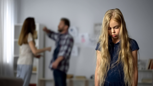 A child looking sad as her parents fight in the background