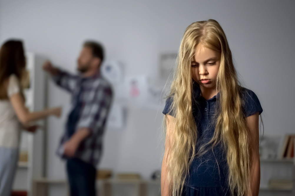 A child looking sad as her parents fight in the background