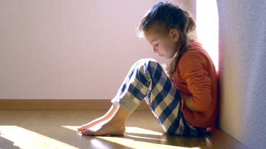 A girl sitting against a wall looking downcast