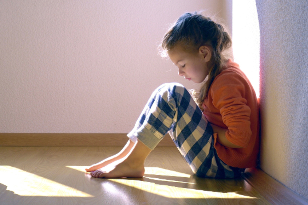 A girl sitting against a wall looking downcast