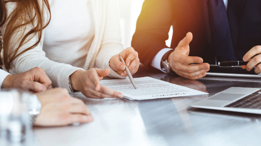 Two Men And A Woman Involved In A Negotiation Meeting Discussing A Document That Is On A Table In Front Of Them